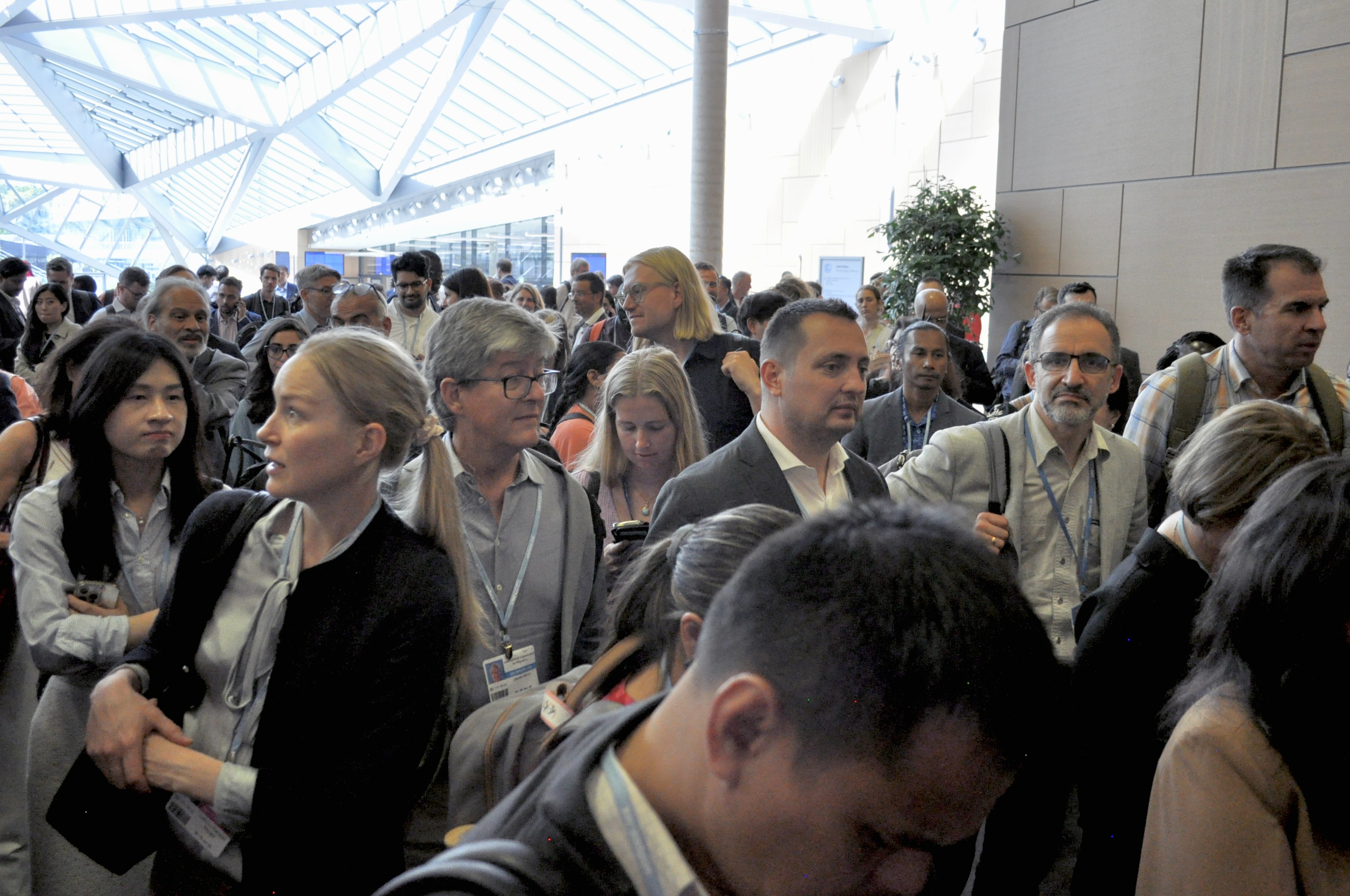 [14] Negotiators and their staff gather at the entrance of a meeting room. In the late afternoon, some use the opportunity to network, while others stand tiredly. 